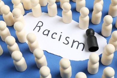 Photo of Card with word Racism and human figures of different colors on blue background, closeup