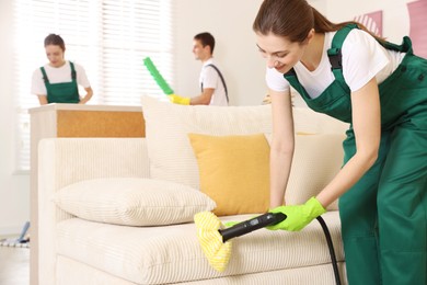 Photo of Professional janitor steam cleaning sofa in room