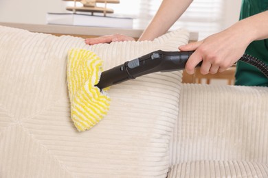 Photo of Professional janitor steam cleaning sofa in room, closeup