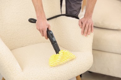 Photo of Professional janitor steam cleaning armchair in room, closeup