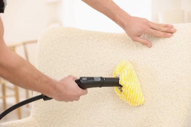 Photo of Professional janitor steam cleaning armchair in room, closeup