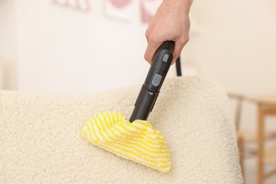 Photo of Professional janitor steam cleaning armchair in room, closeup