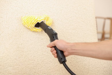 Photo of Professional janitor steam cleaning armchair in room, closeup