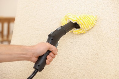 Photo of Professional janitor steam cleaning armchair in room, closeup