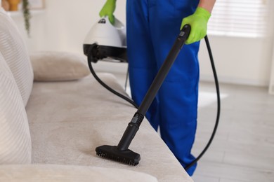 Photo of Professional janitor cleaning sofa with vapor steam system at home, closeup