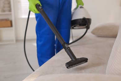 Photo of Professional janitor cleaning sofa with vapor steam system at home, closeup