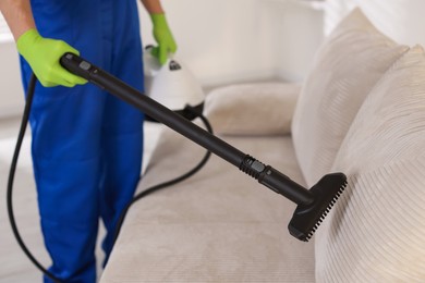 Photo of Professional janitor cleaning sofa with vapor steam system at home, closeup