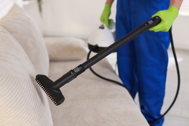 Photo of Professional janitor cleaning sofa with vapor steam system at home, closeup