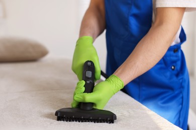 Photo of Professional janitor cleaning sofa with vapor steam system at home, closeup