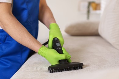 Photo of Professional janitor cleaning sofa with vapor steam system at home, closeup