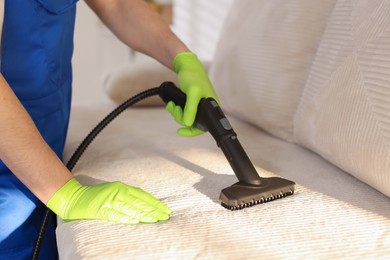 Photo of Professional janitor cleaning sofa with vapor steam system at home, closeup