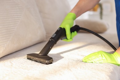 Photo of Professional janitor cleaning sofa with vapor steam system at home, closeup