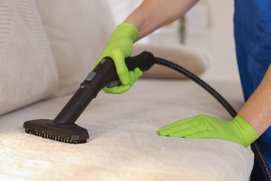 Photo of Professional janitor cleaning sofa with vapor steam system at home, closeup