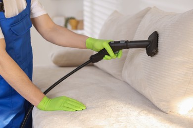 Photo of Professional janitor cleaning sofa with vapor steam system at home, closeup