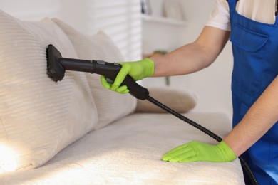 Photo of Professional janitor cleaning sofa with vapor steam system at home, closeup