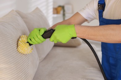 Photo of Professional janitor cleaning sofa with vapor steam system at home, closeup