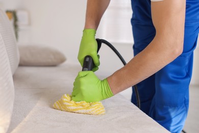 Photo of Professional janitor cleaning sofa with vapor steam system at home, closeup