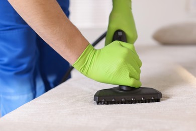 Photo of Professional janitor cleaning sofa with vapor steam system at home, closeup