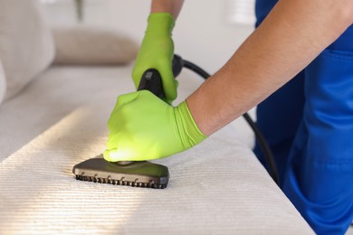 Photo of Professional janitor cleaning sofa with vapor steam system at home, closeup