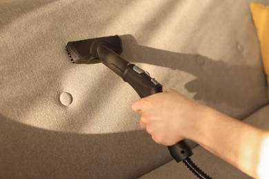 Photo of Professional janitor cleaning sofa with vapor steam system at home, closeup