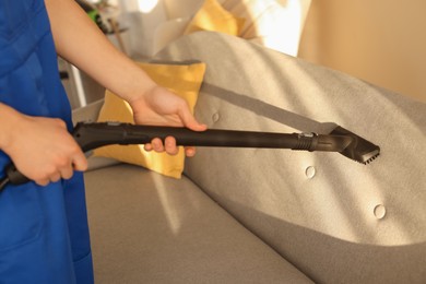 Photo of Professional janitor cleaning sofa with vapor steam system at home, closeup