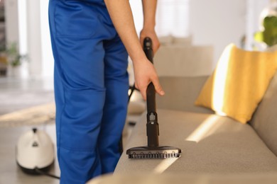 Photo of Professional janitor cleaning sofa with vapor steam system at home, closeup