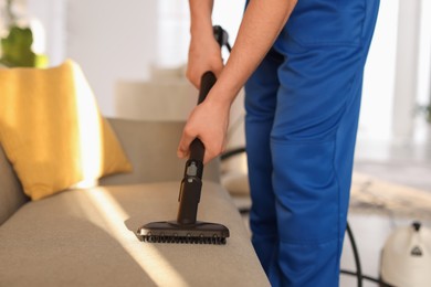 Photo of Professional janitor cleaning sofa with vapor steam system at home, closeup