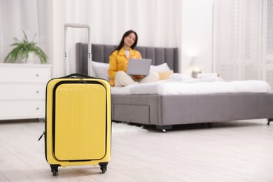 Photo of Suitcase and woman with laptop on bed in her hotel room, selective focus