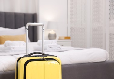 Photo of Stylish suitcase near bed in hotel room, closeup. Space for text