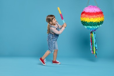 Photo of Happy girl breaking bright pinata with stick on light blue background