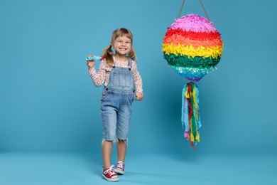 Photo of Happy girl with bright pinata and stick on light blue background