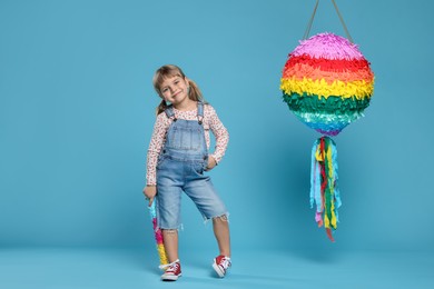 Photo of Cute girl with bright pinata and stick on light blue background