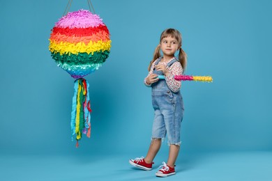 Photo of Cute girl with bright pinata and stick on light blue background