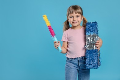 Photo of Happy girl with bright pinata and stick on light blue background. Space for text