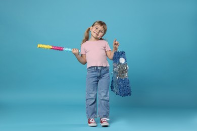 Photo of Happy girl with bright pinata and stick on light blue background