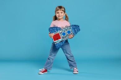 Photo of Cute girl with rocket shaped pinata on light blue background