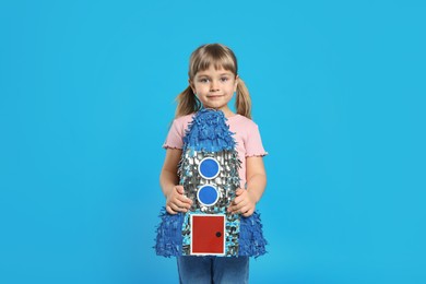 Photo of Cute girl with rocket shaped pinata on light blue background