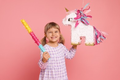 Photo of Happy girl with unicorn shaped pinata and stick on pink background