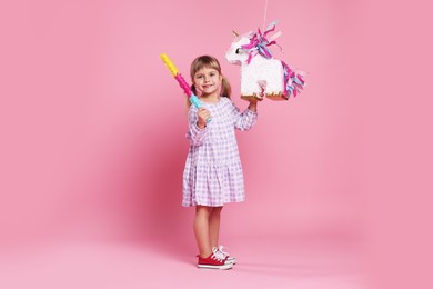 Photo of Happy girl with unicorn shaped pinata and stick on pink background