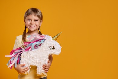 Photo of Happy girl with unicorn shaped pinata on orange background. Space for text