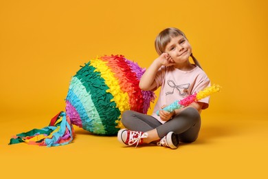 Photo of Cute girl with bright pinata and stick on orange background