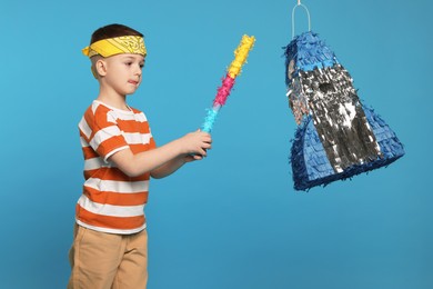 Photo of Cute boy breaking rocket shaped pinata with stick on light blue background