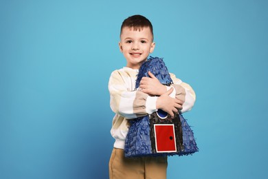 Photo of Happy boy with rocket shaped pinata on light blue background