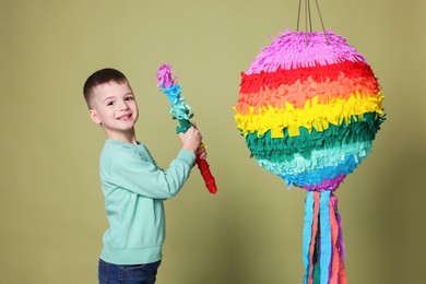 Photo of Happy boy breaking colorful pinata with stick on olive color background