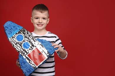 Photo of Happy boy with rocket shaped pinata on red background. Space for text