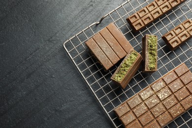 Photo of Delicious Dubai chocolate bars with pistachios and knafeh on black table, top view. Space for text