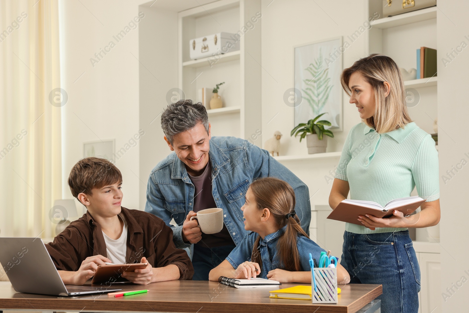 Photo of Happy parents and their children doing homework with laptop at table indoors