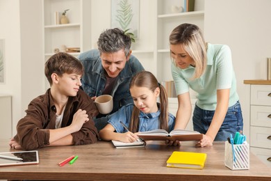 Photo of Parents and their children doing homework at table indoors