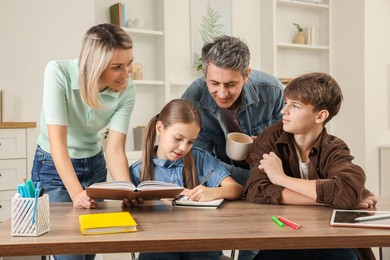 Photo of Parents and their children doing homework at table indoors