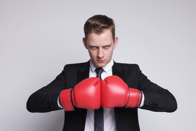 Photo of Competition. Businessman in suit wearing boxing gloves on grey background